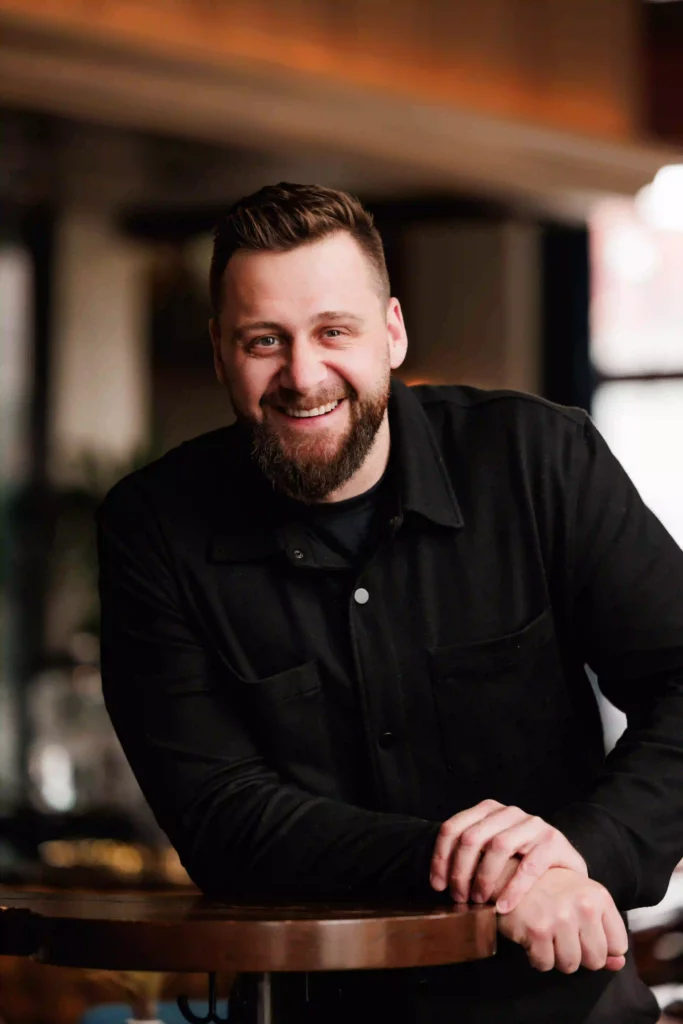 Professional portrait of Jay Catlin, founder of Catlin Design Build, smiling in a modern interior setting while wearing a black button-up shirt.
